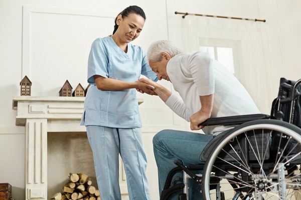 Medical assistance. Pleasant good looking senior man holding caregivers hand and getting up from the wheelchair while staying at the nursing home